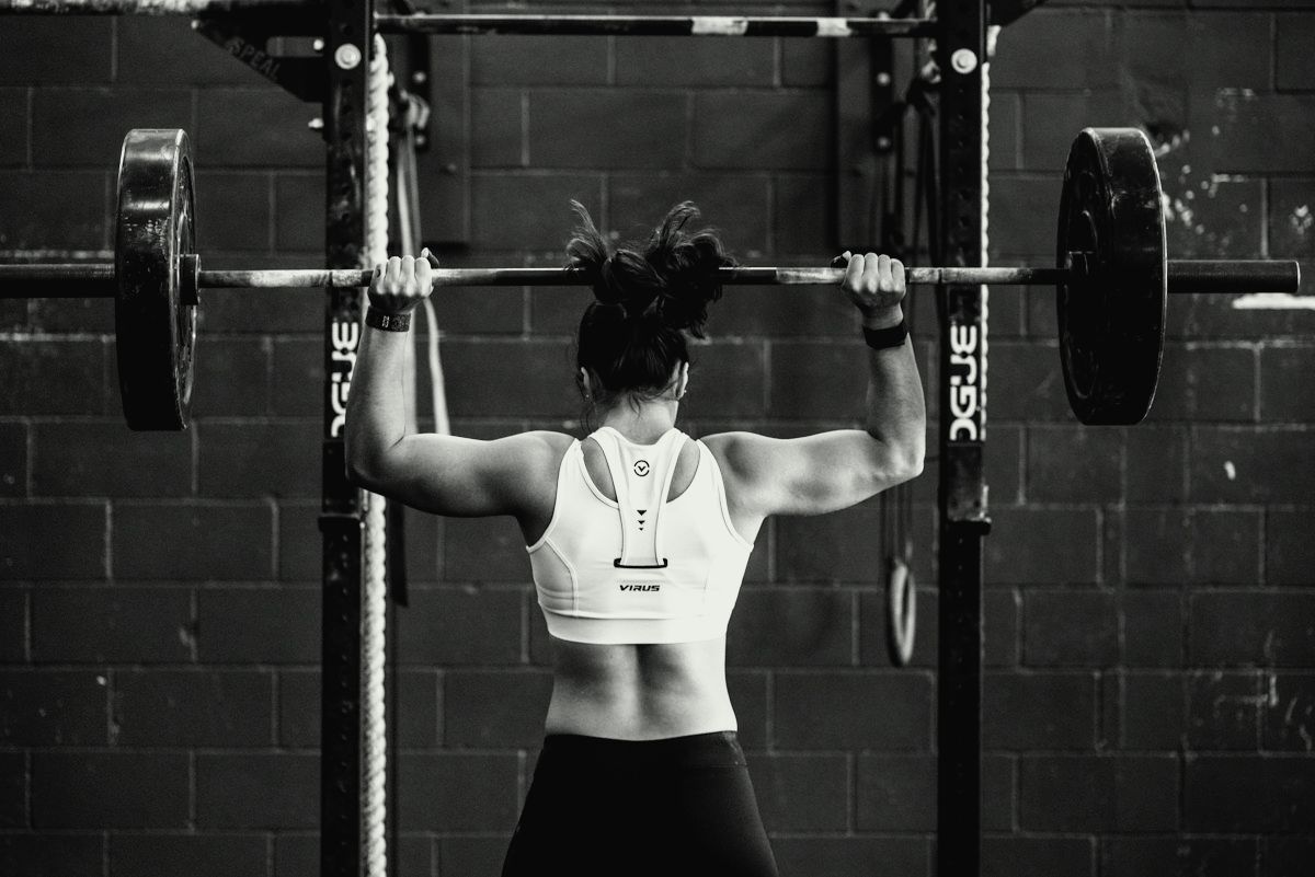 A woman pressing a barbell overhead in a squat rack
